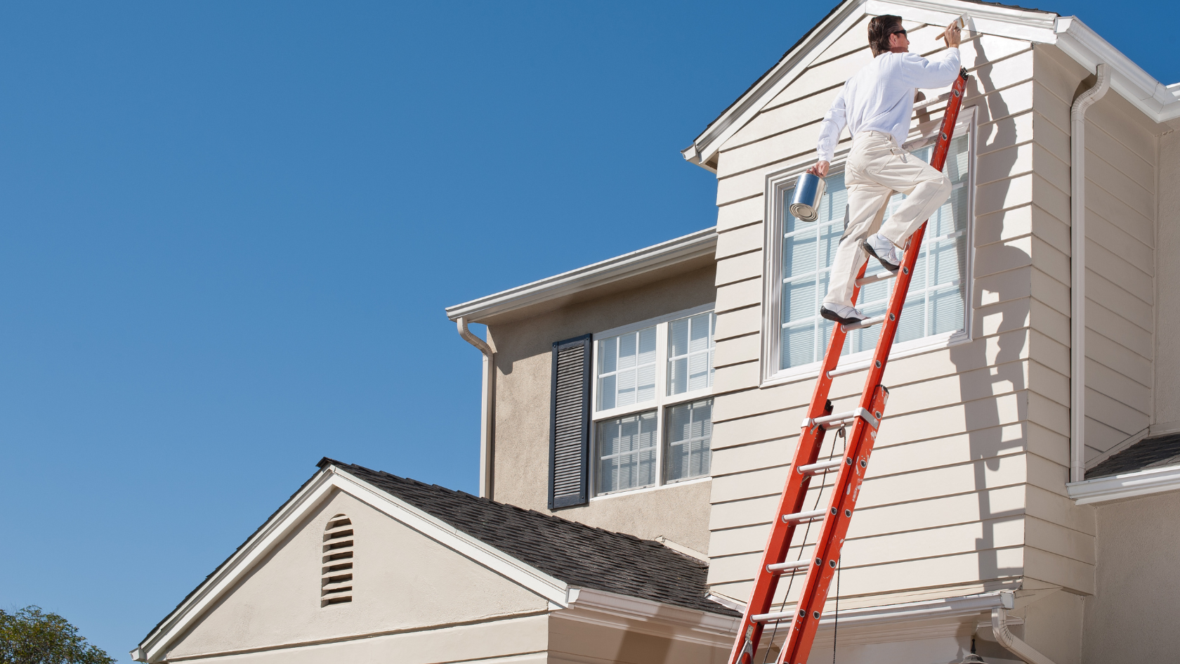 A man on a ladder painting the side of a house